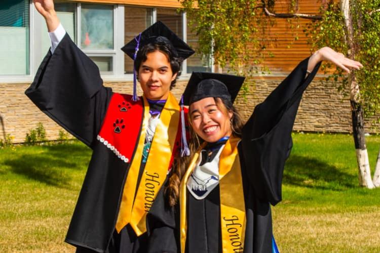 Two students wearing honours grad regalia celebrating outdo或s
